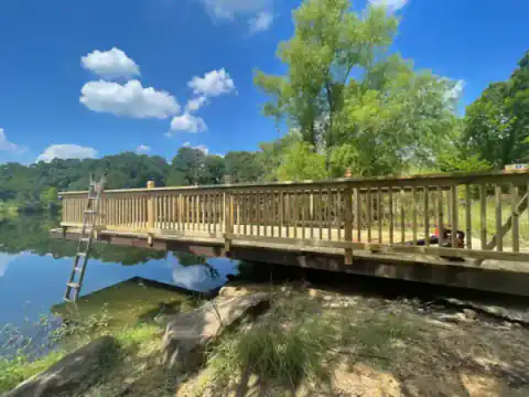 Wood footbridge crosses a pond beside a fenced property.