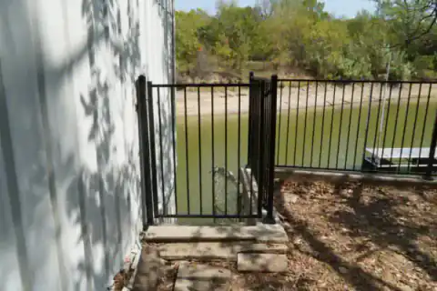 Black metal pedestrian gate secures a backyard pool area.