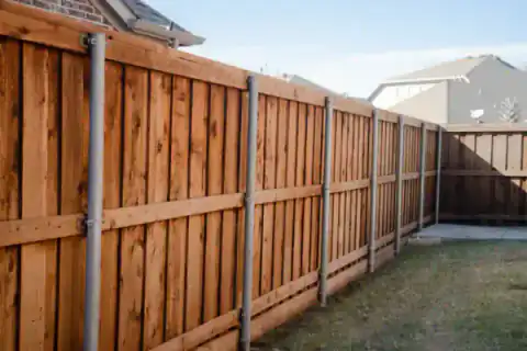 Cedar privacy fence runs beside a brick residential home.