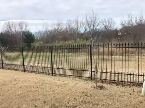 Black metal fence defines an open North Texas lot.