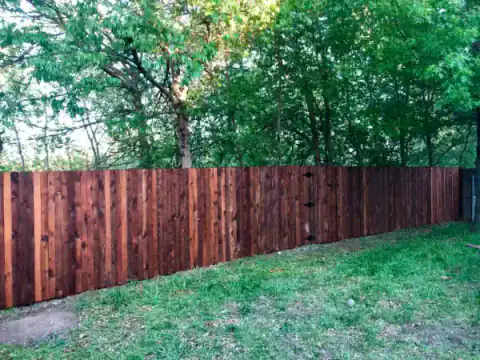 Red cedar privacy fence runs beneath mature shade trees.