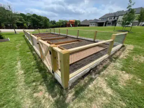 Wood-framed animal enclosure with gates fills a grassy field.