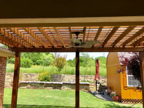Open-beam cedar pergola frames a brick home's outdoor room.