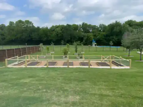 Wood-framed animal enclosure with gates fills a grassy field.