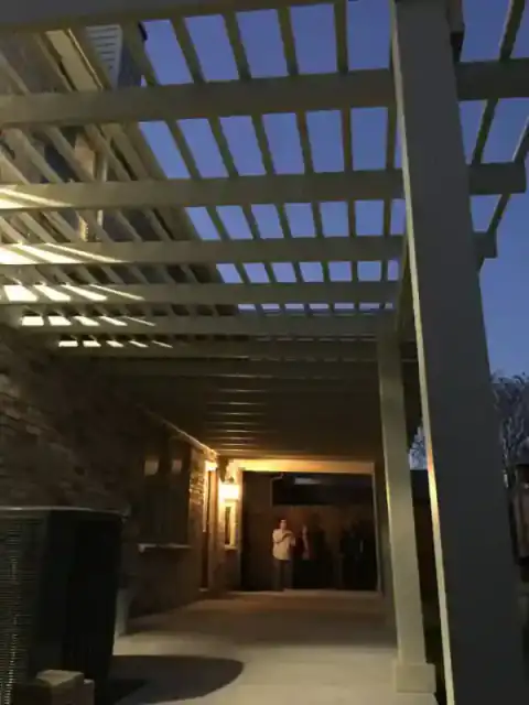 Covered patio walkway glows beneath a dark pergola roof.