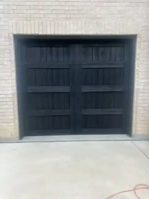 Dark carriage-style garage door set in a pale brick facade
