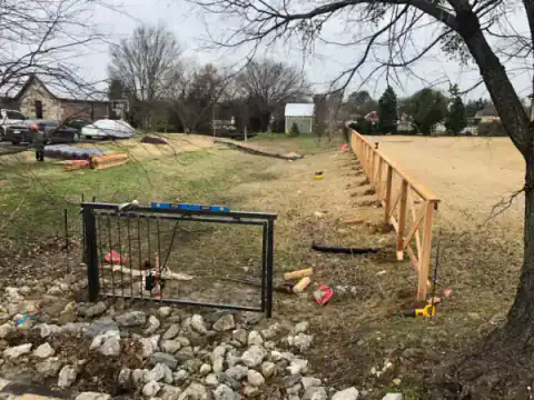 Black metal gate fronts a rock-lined drainage channel.