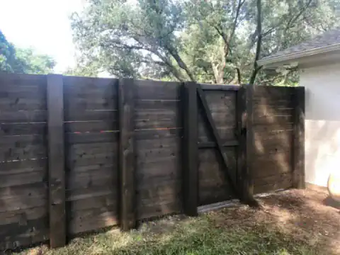 Dark cedar gate with a diagonal brace closes a side yard.