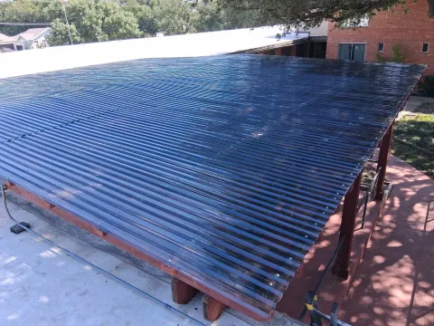 A large custom patio cover with translucent corrugated roofing over a sturdy timber frame, letting natural light through while blocking the weather.