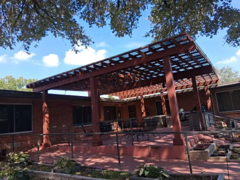 A stained timber pergola with a translucent roof panel system shading a residential brick patio.