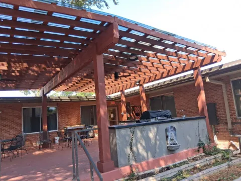 A custom wood pergola with integrated lighting and a ceiling fan over an outdoor kitchen and lounge area.