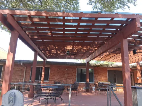 A cedar pergola with a translucent roof, ceiling fan, and cable railings installed against a brick exterior.