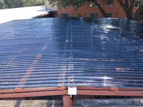 An overhead view of a completed patio cover with translucent polycarbonate panels installed over a wood frame.